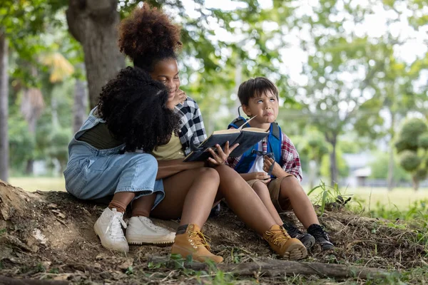 children African American ethnicity sitting to their sisters reading a book in the park