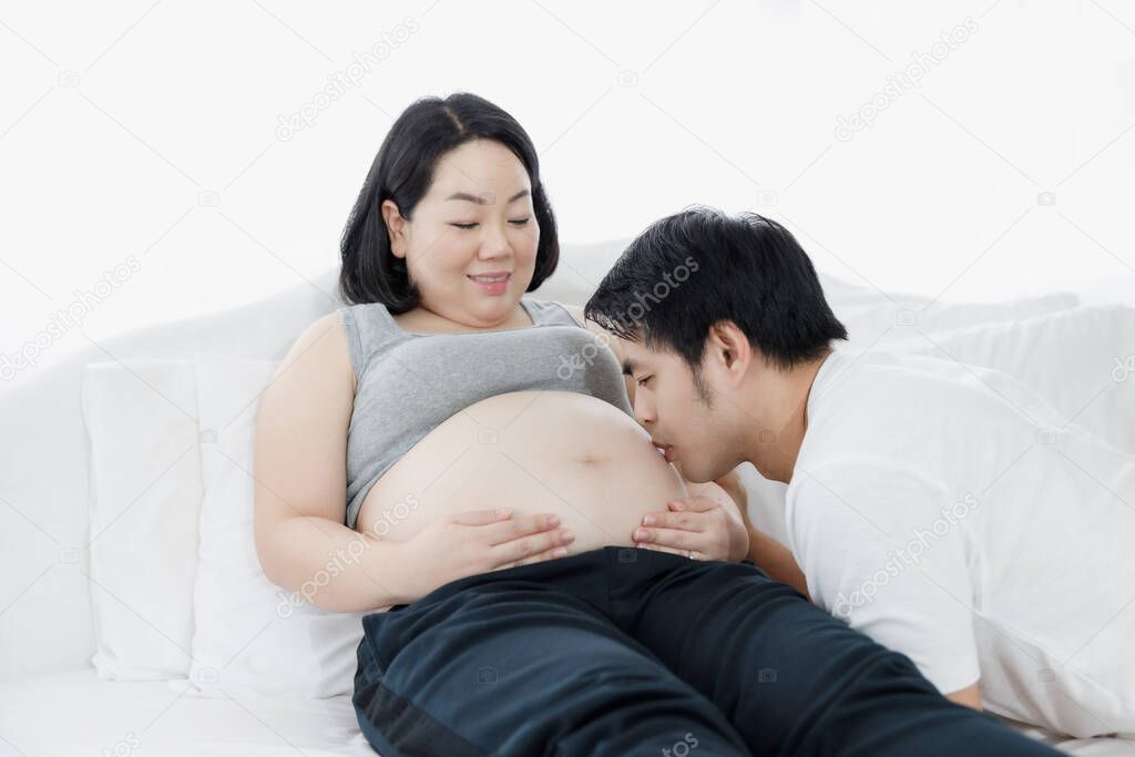 Young happy beautiful pregnant couple Handsome asian man kissing the bare belly of his pregnant wife. love and family concept