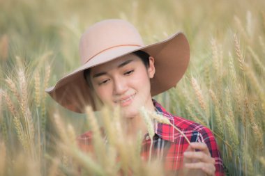 Ekose gömlekli ve şapkalı genç Asyalı çiftçi kız seçici odaklı akıllı çiftçi konseptiyle arpa pirinç portresinin portresini kontrol ediyor. 
