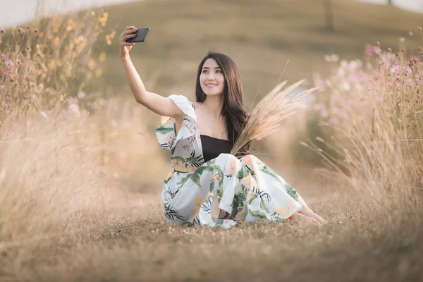 美丽的亚洲女人坐在智能手机上自私自利 牵着绿草的手 是公园里花卉图片风格的老古董 — 图库照片