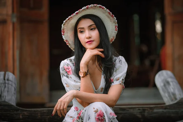 レトロな花ピンクのドレススタイルと帽子ヴィンテージ木製の階段フロントビューに座っている美しい若いアジアの女性古い家の背景と見下ろす 休暇やレトロなスタイルのアイデアで自然な光の肖像画のプロフィール — ストック写真