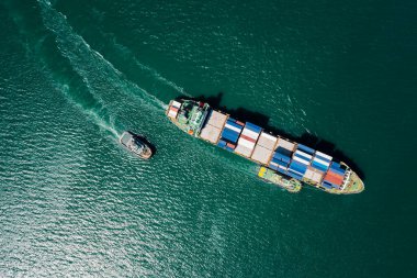 container ship and tugboat dragging line in green sea aerial top view from drone 