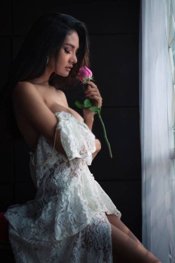 Sanat sevdası konsepti. Beyaz elbiseli Asyalı genç kadın ve koyu arkaplanda gül.