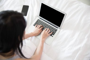 Yatak odasındaki beyaz yatakta dizüstü bilgisayar kullanan kadın ev fotoğrafı yumuşak odaklı spor yapıyor.