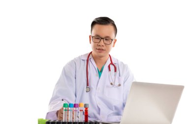 Masanın üzerinde kan örneği ve dizüstü bilgisayarı olan Taylandlı bir doktor.