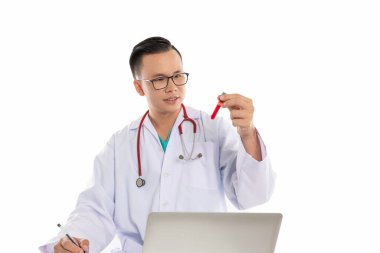 Masanın üzerinde kan örneği ve dizüstü bilgisayarı olan Taylandlı bir doktor.