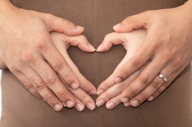 Çift, hamile karnına kalp şeklinde bebek bakımı konsepti yerleştiriyor. Yaklaş ve seçici odaklan.