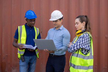 Lojistik depo ustabaşısı dizüstü bilgisayarla konuşuyor ve kadın işçiler ithalat ticaret hizmetleri kargosundaki konteynır kutularının listesini kontrol ediyor.