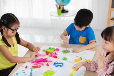 Asyalı çocuklar okul konseptine dönmek için yaz mevsiminde masada kil rengi oynuyorlardı.