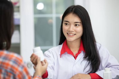 Asyalı kadın eczacı ilacı nasıl kullanacağını anlatıyor, reçeteyi elinde tutuyor ve eczanedeki müşteriyle konuşuyor, eczacı Asyalı hasta Tayland 'a ilaç gönderiyor.