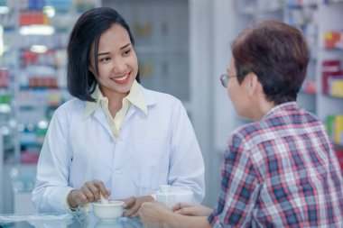 Tayland 'da bir eczanede kadın hastalara reçeteli ilaçları açıklayan Asyalı kadın eczacı ya da doktor. 