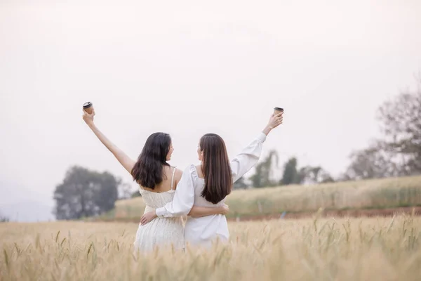 两个身穿服饰的亚洲女孩站在后面 在大麦田里拿着纸杯咖啡 自由旅行的生活方式 在泰国昌麦的游园地里展示 — 图库照片