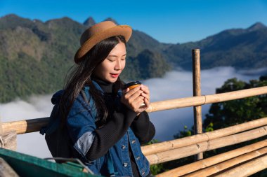 Asyalı kadın sırt çantalı özgürlük gezisi sabah kahve fincanı ve dağ sisi içerek mavi gökyüzü manzaralı arka plan Chiang Mai Tayland manzaralı