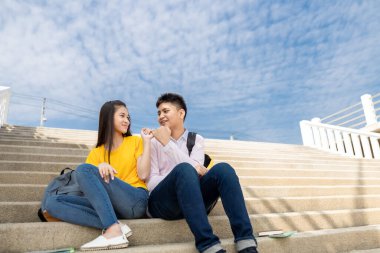 Erkek ve kız arkadaş el ele tutuşup parktaki merdivenlerde gülümsüyorlar yaz öğrencileri konseptinde.