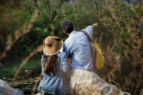 年轻的亚洲夫妇游客坐在河边自然林的岩石上 手牵着手看着自然林 — 图库照片