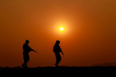 Siluet aksiyon askerleri kampa geri dönüyor ve silah taşıyorlar. Günbatımı beyaz denge gemisinin etkisi. 