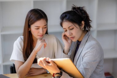 Tablet kullanan iki genç Asyalı kadın, modern ofiste oturup sosyal ağda mesaj yazarak sohbet ediyorlar. Konsept, Onlin 'de çalışan blogger serbest yazarına odaklanmış durumda.