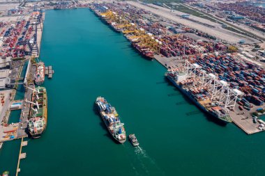 Deniz ve ticari limanda seyir halindeki hava manzaralı konteynır gemisi ve römorkör ithalat, nakliye veya ulaşım kavramı için vinç köprüsü yükleme konteynırı