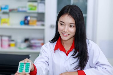 young asian female pharmacist smiling and selling vitamins and medicines capsule to the customer in pharmacy shop thailand 