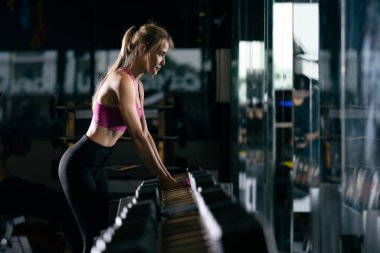 Spor ayakta duran seksi kadınlar spor salonunda dambıllarla ve sinematik ses tonuyla çalışıyorlar. 