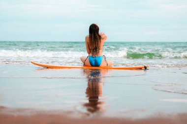 Sörf tahtasında oturan ve tropikal bir yerde poz veren güzel Asyalı kız yaz tatilinde deniz konseptinde rahatlıyor.