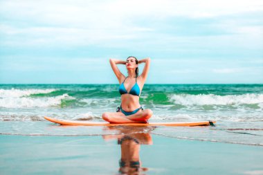 Sörf tahtasında oturan ve tropikal bir yerde poz veren güzel Asyalı kız yaz tatilinde deniz konseptinde rahatlıyor.