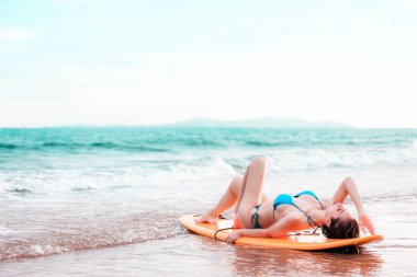 Sörf tahtasına uzanmış güzel Asyalı kız tropik bir yerde, kumsalda poz veriyor, yaz tatilinde seyahat ediyor deniz konseptinde rahatlıyor.