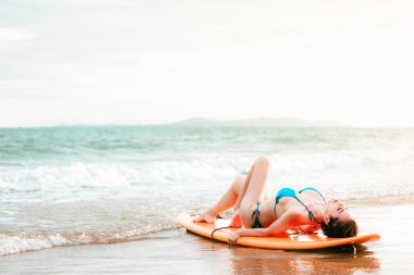 Sörf tahtasına uzanmış güzel Asyalı kız tropik bir yerde, kumsalda poz veriyor, yaz tatilinde seyahat ediyor deniz konseptinde rahatlıyor.