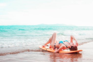 Sörf tahtasına uzanmış güzel Asyalı kız tropik bir yerde, kumsalda poz veriyor, yaz tatilinde seyahat ediyor deniz konseptinde rahatlıyor.