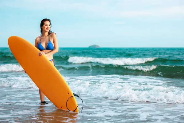 Sörf tahtasıyla ayakta duran ve tropik bir yerde poz veren Asyalı güzel bir kız yaz tatili seyahatinde deniz konseptinde rahatlar.