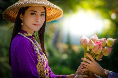 Vietnamlı mor elbiseli, arkasında pembe nilüfer çiçeği olan Tayland mankenleri.