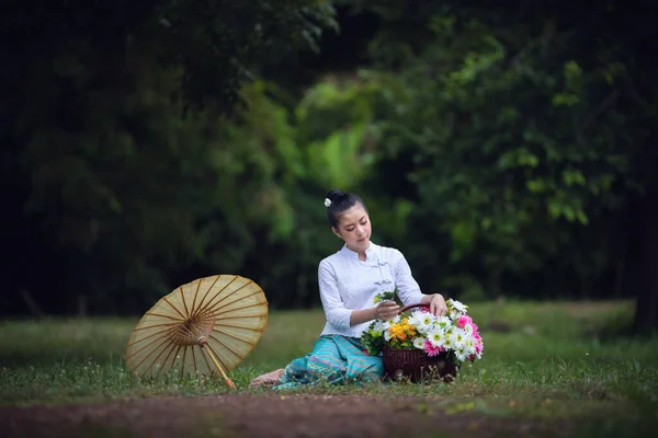 在泰国北部 年轻的亚洲女孩穿着当地的衣服 带着雨伞 绿色的公园里开着花 — 图库照片