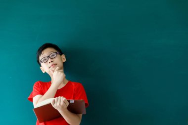 Asyalı çocuk elinde kitap tutuyordu. Yaz mevsiminde uzay sınıfında yeşil tahtanın önünde duruyordu. Okul konseptine geri dönüyordu.