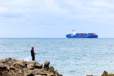 Kaya ve konteynır gemisinde duran balıkçı deniz bulutu arka planında yelken açıyor.