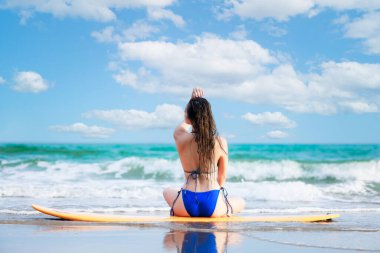 asian girl sitting back posing with her surfboard on the beach in summer blue tone process,