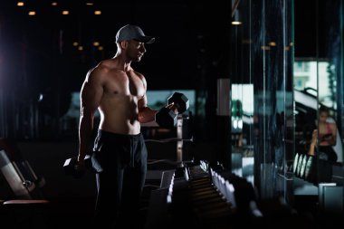 muscular man working out with dumbbells in gym dark tone, 