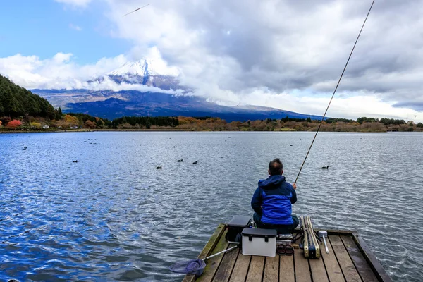 Landscape of A Man Sit and Fishing Alone on wooden bridge at Kawaguchiko Lake in Japan during Sunset with Fuji Mountain Background