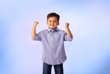 Erkek çocuk stüdyo fotoğrafında mavi arka planda gömlek ve kot pantolon giyiyor..