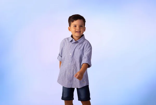 Erkek çocuk stüdyo fotoğrafında mavi arka planda gömlek ve kot pantolon giyiyor..