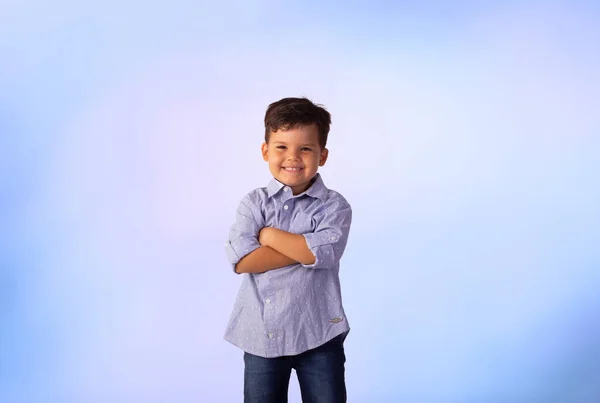 Erkek çocuk stüdyo fotoğrafında mavi arka planda gömlek ve kot pantolon giyiyor..