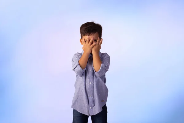 Erkek çocuk stüdyo fotoğrafında mavi arka planda gömlek ve kot pantolon giyiyor..