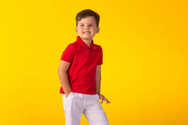 Kırmızı polo tişörtlü çocuk, beyaz şort ve sarı arka planlı stüdyo fotoğrafı..