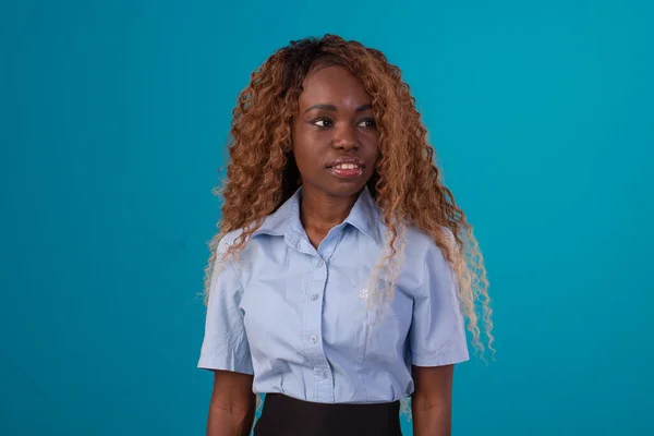 Stüdyo fotoğrafında kıvırcık saçlı, mavi gömlekli, siyah etekli ve değişik yüz ifadeleri takınan siyah bir kadın..