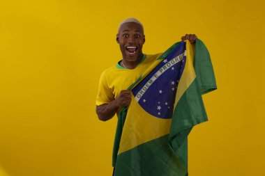 Brezilya bayrağını tutan siyah tenli bir adam ve stüdyo fotoğrafında Brezilya futbol takımının gömleğini giyiyor.