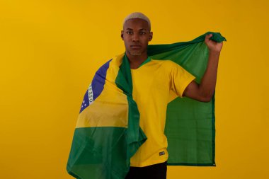 Brezilya bayrağını tutan siyah tenli bir adam ve stüdyo fotoğrafında Brezilya futbol takımının gömleğini giyiyor.