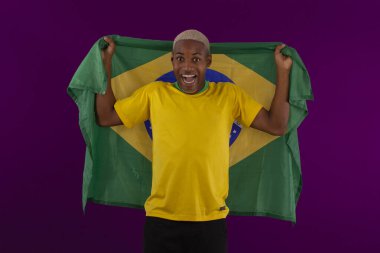 Brezilya bayrağını tutan siyah tenli bir adam ve stüdyo fotoğrafında Brezilya futbol takımının gömleğini giyiyor.