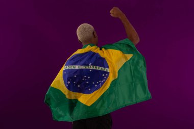 Brezilya bayrağını tutan siyah tenli bir adam ve stüdyo fotoğrafında Brezilya futbol takımının gömleğini giyiyor.