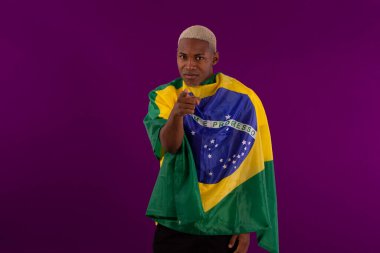 Brezilya bayrağını tutan siyah tenli bir adam ve stüdyo fotoğrafında Brezilya futbol takımının gömleğini giyiyor.