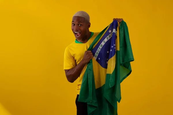 Brezilya bayrağını tutan siyah tenli bir adam ve stüdyo fotoğrafında Brezilya futbol takımının gömleğini giyiyor.