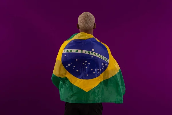 Brezilya bayrağını tutan siyah tenli bir adam ve stüdyo fotoğrafında Brezilya futbol takımının gömleğini giyiyor.